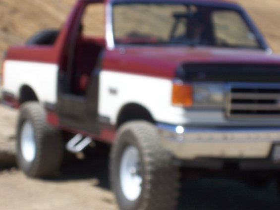 Two-tone red and white Ford Bronco with doors removed, lifted suspension, and off-road tires