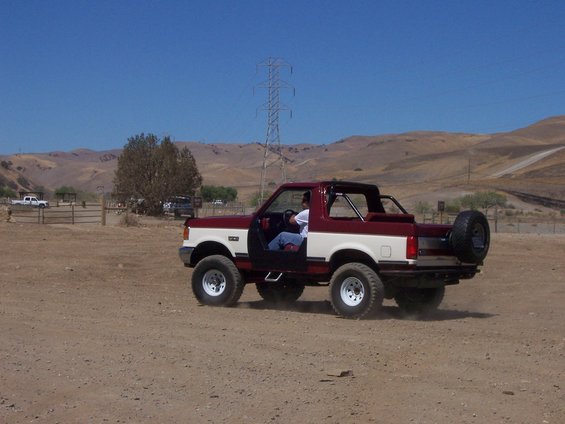 Red and white 1991 Ford Bronco with doors removed, driving on a dirt road