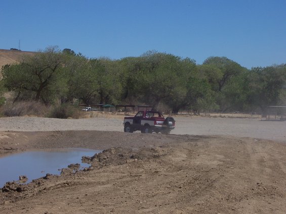 Red and white Ford Bronco with a spare tire on the back, driving on a dirt road