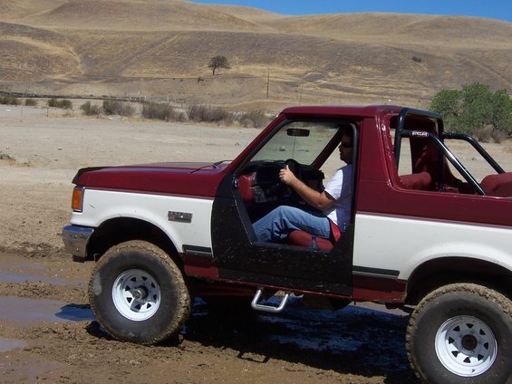 1991 Ford Bronco with doors removed, driving through mud