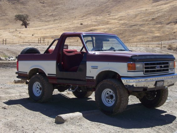 Maroon and white Ford Bronco with off-road tires and spare tire on back