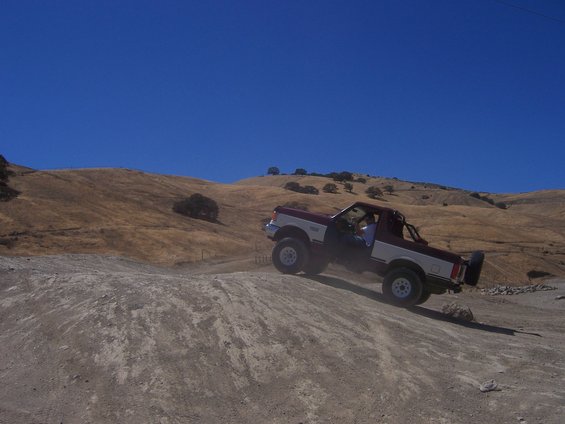 Two-tone Ford Bronco driving up a dirt hill