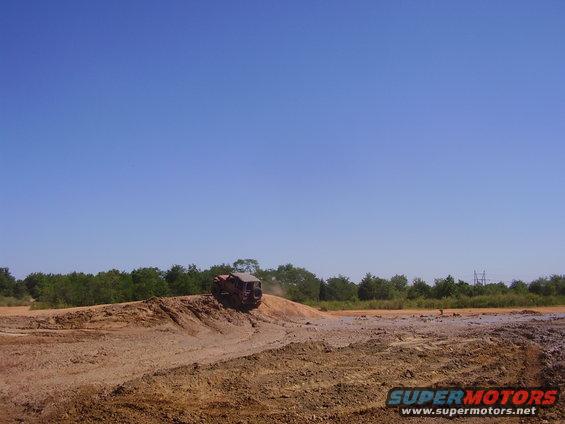 Off-road vehicle climbing a dirt mound under a clear blue sky