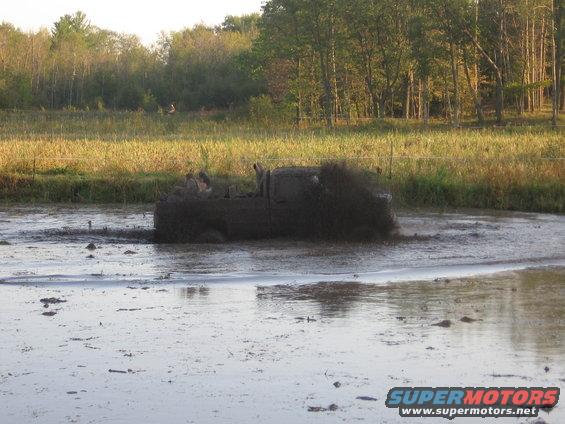 Dark-colored pickup truck splashing mud while driving through a muddy field
