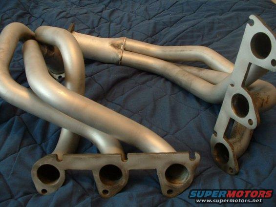 Exhaust manifold pipes with two mounting flanges, silver metal, on a blue quilted surface
