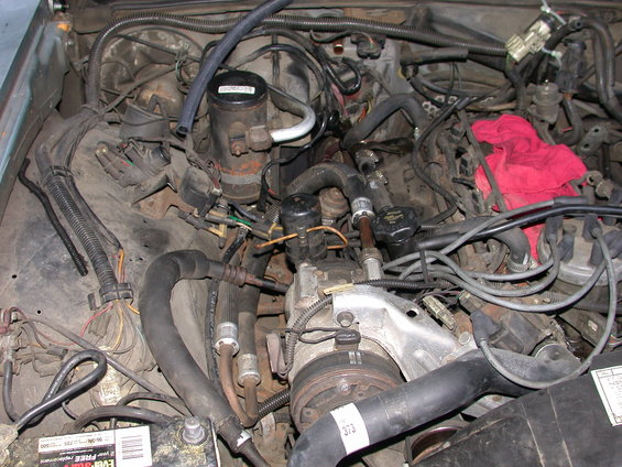 Engine bay with lots of hoses, wires, and engine parts. A red rag is on top of some components