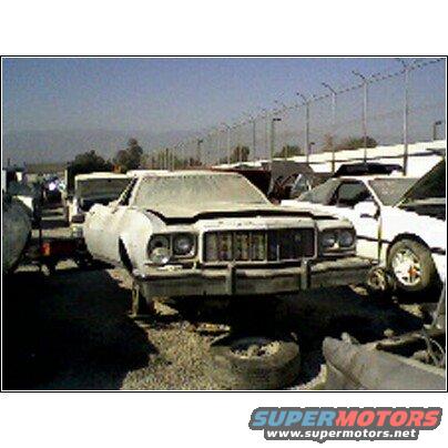 White 1974 Ford Ranchero in junkyard, front view, hood up, dusty, on blocks