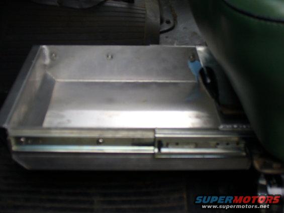Metal slide-out storage tray with visible drawer slides, next to a green seat