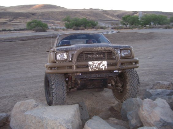 Mud-covered Toyota truck with bull bar, driving over rocks