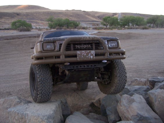 Mud-covered Toyota pickup truck with bull bar, front wheels on rocks