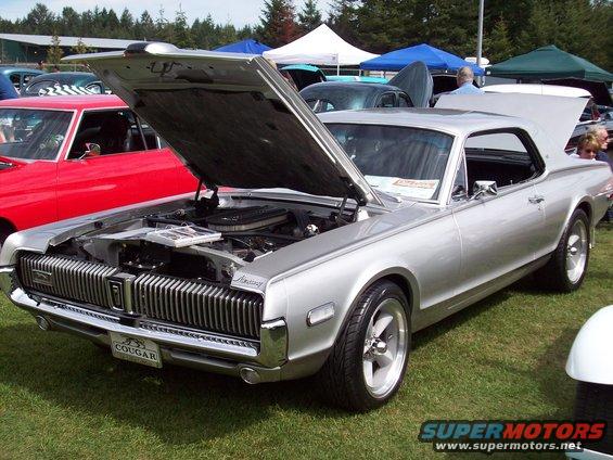Silver 1969 Mercury Cougar with hood and trunk open, parked on grass. Red car visible to the left