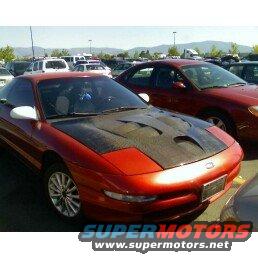 Red coupe with aftermarket hood, 3/4 front view. Another red car behind it