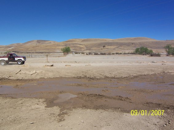 Red and white 1991 Ford Bronco driving through a muddy field