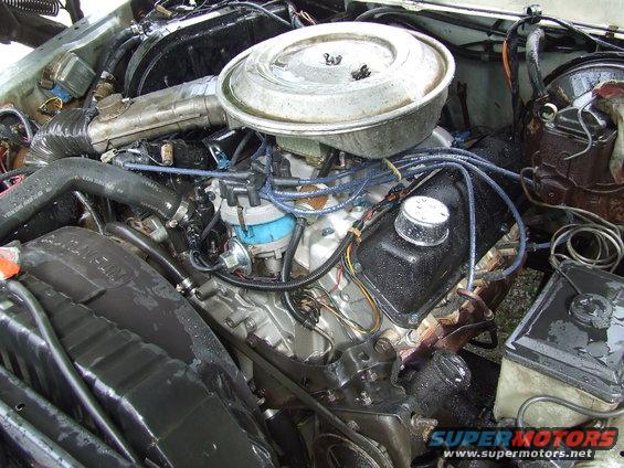 Engine bay with V8 engine, air cleaner, distributor, and hoses. Some parts appear worn