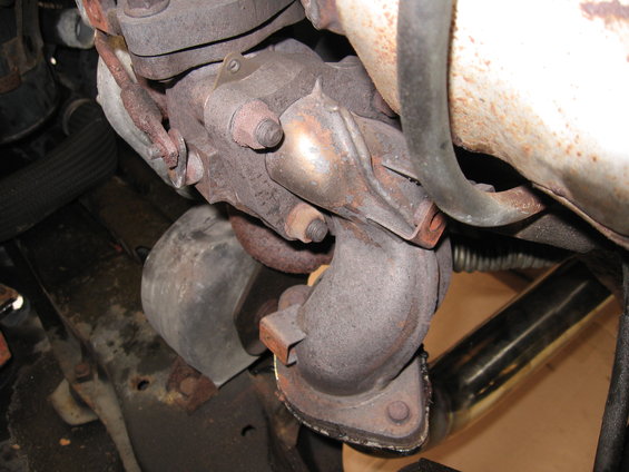Turbocharger and exhaust manifold assembly with rusted metal components and a black hose