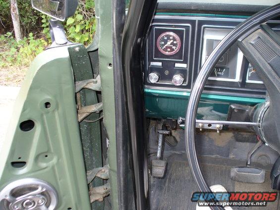 Green vehicle interior showing dashboard gauges, steering wheel, and door hinge