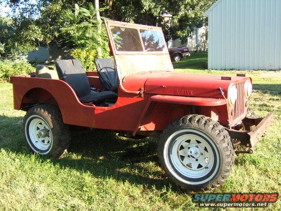 Red Willys Jeep parked on grass, front end visible. Has white rims and black seats
