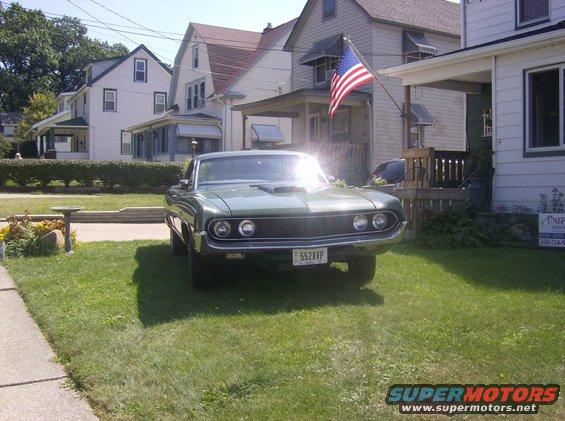 1970 Ford Ranchero parked on a lawn in front of houses, American flag flying