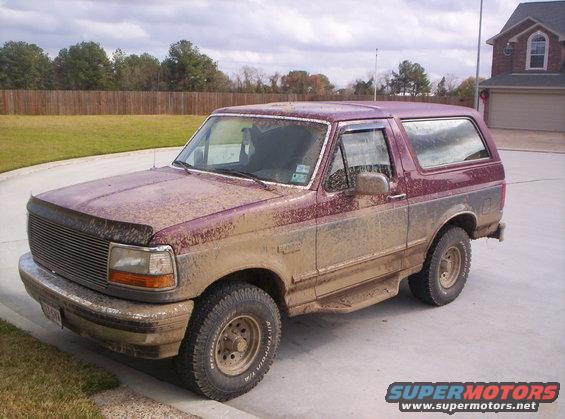 Mud-covered maroon Ford Bronco, 3/4 front view. Visible damage to front bumper and hood