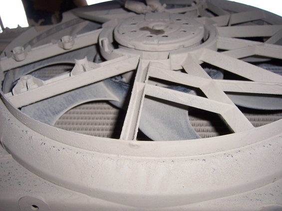Close-up of a dusty white fan shroud over a radiator. The shroud has a complex, angular design