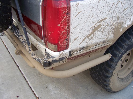 Mud-splattered white pickup truck rear with custom bumper and spare tire