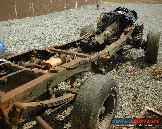 Rusted vehicle frame with engine and transmission, front and rear leaf springs visible