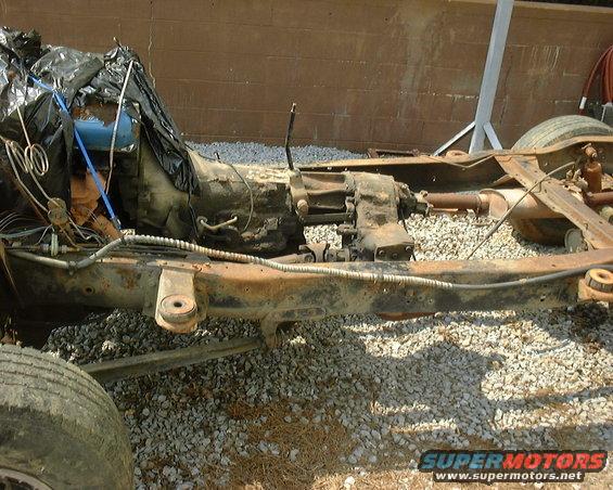 Rusty vehicle chassis with transmission, transfer case, driveshaft, and rear tire visible