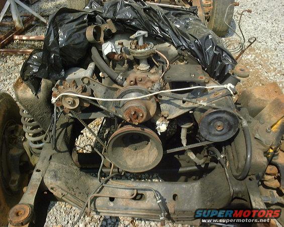 Engine and chassis parts covered in black plastic, with visible belts and pulleys