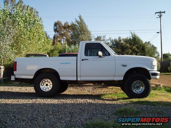 White 1994 Ford F-150 pickup truck, side view, lifted suspension, chrome wheels, parked on gravel