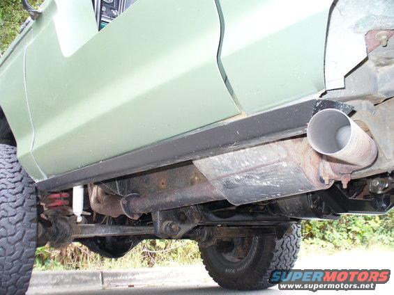 Side view of a light green vehicle's undercarriage, showing the rocker panel, exhaust system, and suspension components
