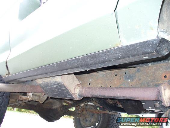 Light green vehicle rocker panel and rusty frame with exhaust pipe visible