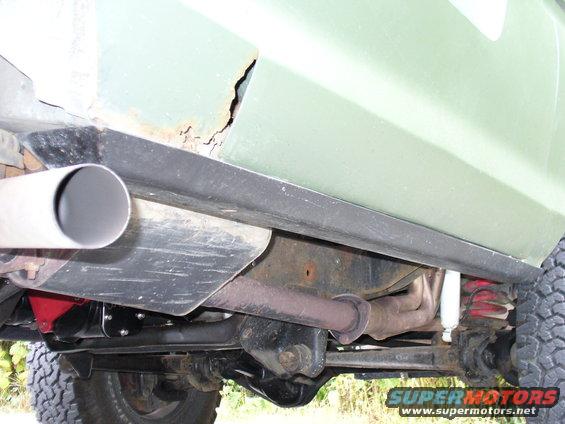 Undercarriage view of light green vehicle with rust, showing exhaust and suspension