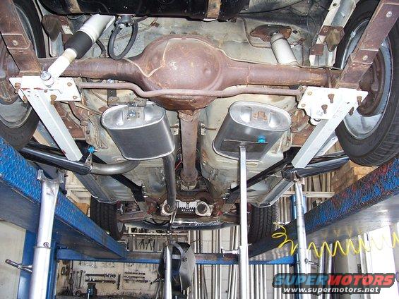 Underside of a car on a lift, showing the rear axle, dual exhaust, and suspension components
