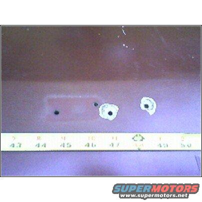 Red tailgate with three holes, two with white primer, measured with a ruler marked in inches