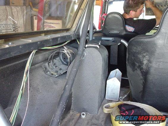 Interior view of a vehicle with a roll cage, racing seats, and exposed wiring