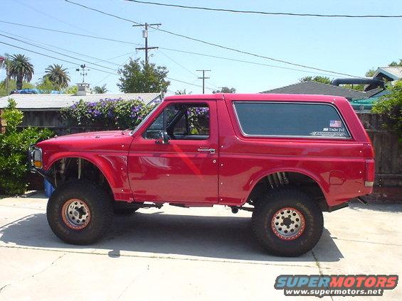 Red lifted SUV parked outside on a sunny day. It has large off-road tires and custom suspension