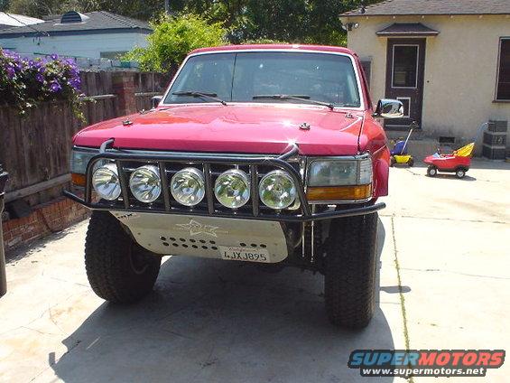 Red Ford Bronco, front view, with aftermarket bumper and four large driving lights. License plate reads 4JXJ895