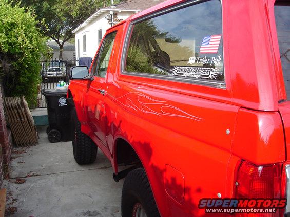 Red Ford Bronco with pinstripe flames on the side and an American flag sticker on the rear window