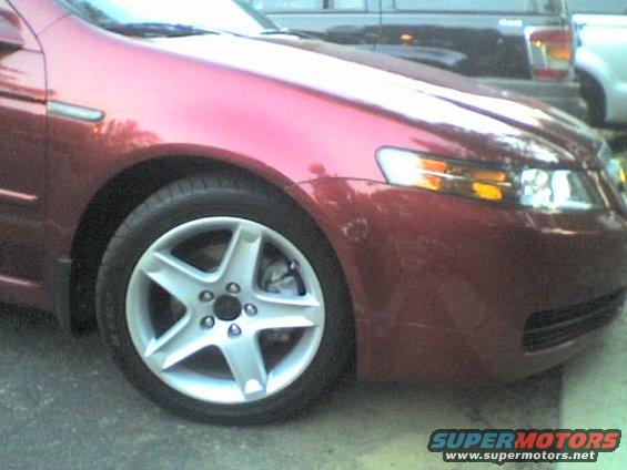 Red car's front quarter panel and five-spoke wheel, with other vehicles in background