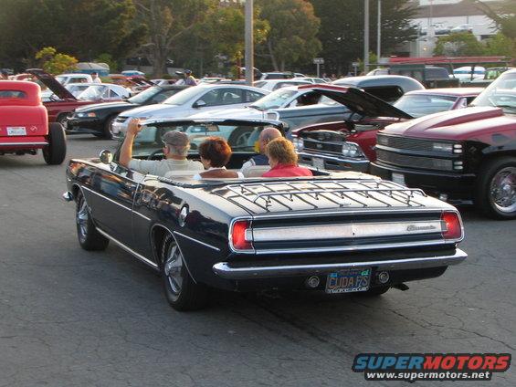 1969 Plymouth Barracuda convertible with a luggage rack on the trunk, driving in a parking lot with other cars