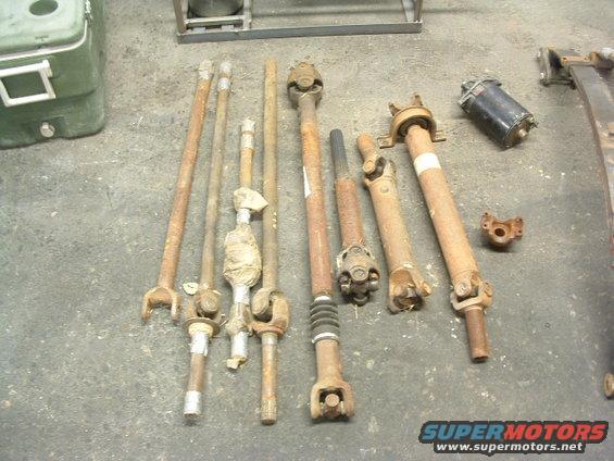 Several driveshafts and a black starter motor laid out on a concrete floor
