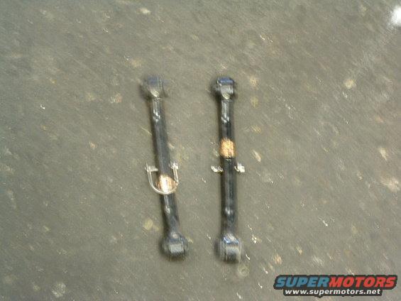 Two black metal suspension control arms with visible wear and a small gold-colored badge on one