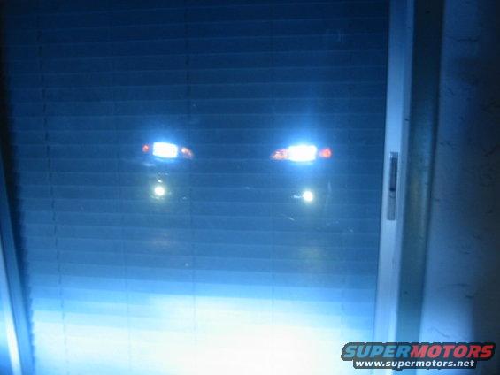 Car headlights glowing through blinds, with a Supermotors.net logo visible at the bottom right