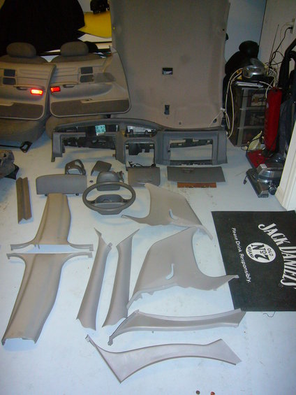 Car interior trim pieces, dashboard, steering wheel, and seats laid out on the floor