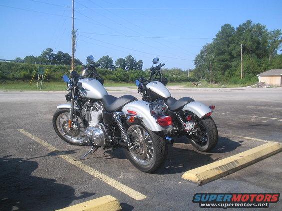 Two silver Harley-Davidson motorcycles parked side-by-side in a paved lot with yellow parking blocks