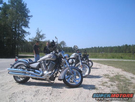 Three Victory motorcycles parked on a dirt road with trees and blue sky in the background