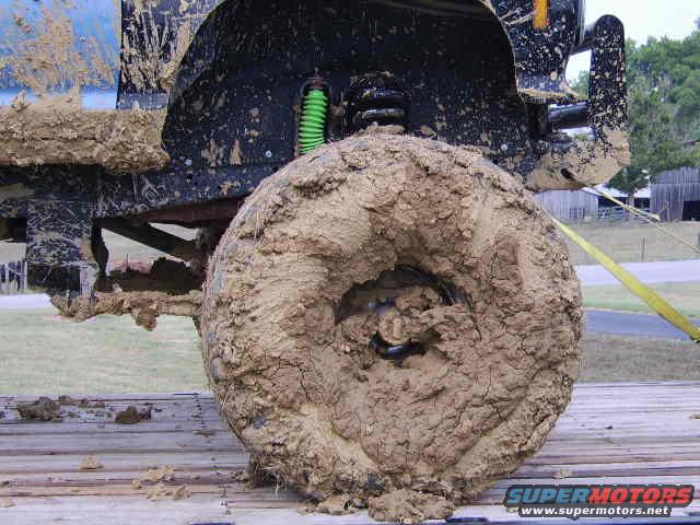Mud-covered truck tire and suspension components, including a green shock absorber