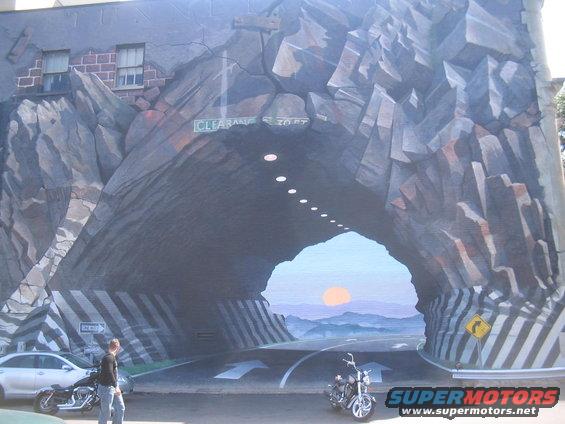 Mural depicting a tunnel with a sign reading 'CLEARANCE 10 FT' and a landscape scene visible through the opening