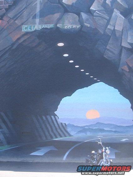 Mural of a motorcycle parked inside a tunnel with a sunset visible at the end. Sign says 'CLEARANCE 30 FT'