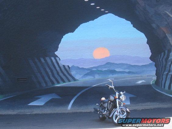 Gray motorcycle parked in front of a tunnel opening with a sunset and mountains